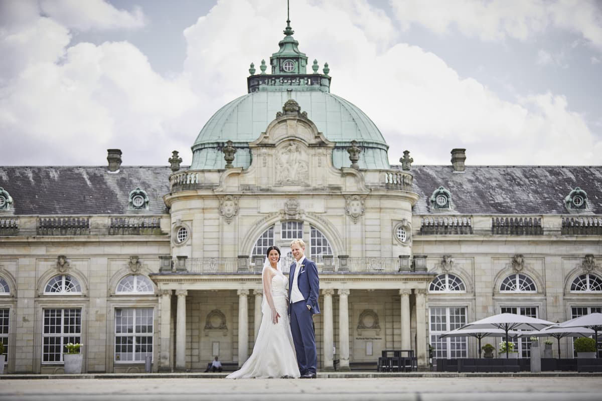 Lächelndes Brautpaar vor dem Kaiserpalais in Bad Oeynhausen mit grüner Kuppel – Hochzeitsfoto vor historischer Kulisse
