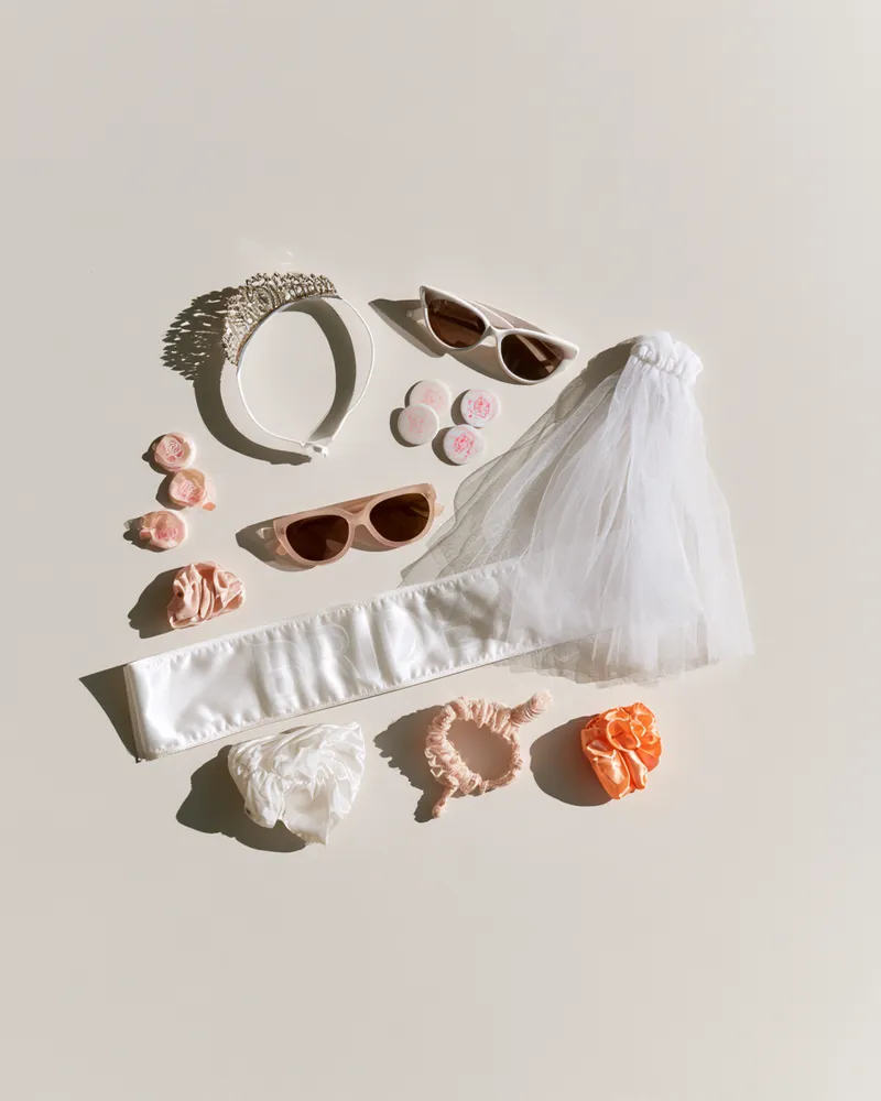 JGA-Accessoires von oben: Schärpe mit „Bride“-Aufdruck, Schleier, Diadem, Sonnenbrillen, Buttons und Haargummis für den Junggesellinnenabschied