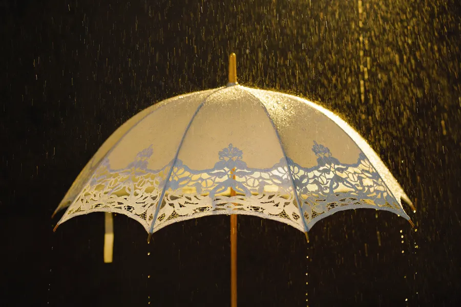 Brautpaar unter elegantem weißem Hochzeitsschirm im Regen